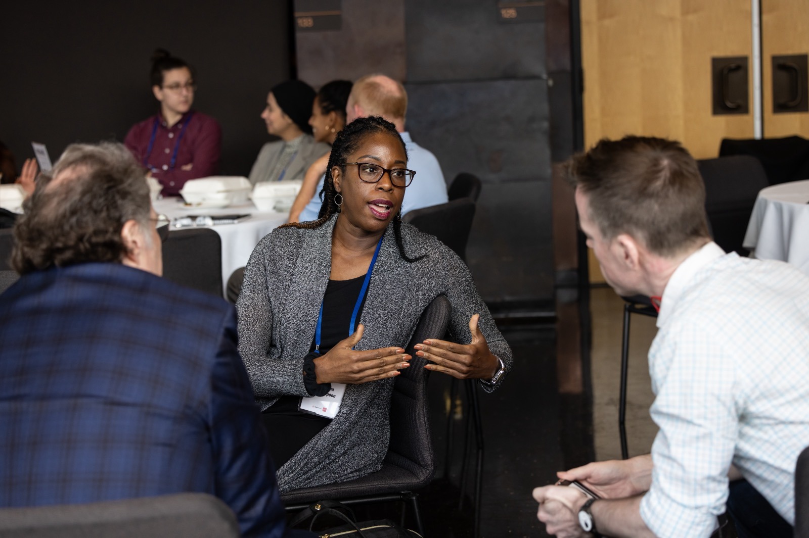 Woman talks to two people at a conference table with other people in the background